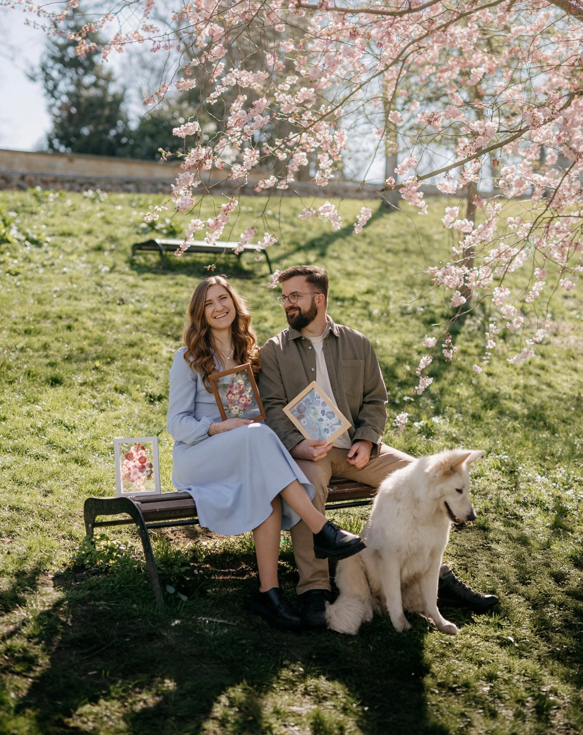 Zakladatelé LissWood se psem na lavičce pod rozkvetlou třešní drží své obrazy