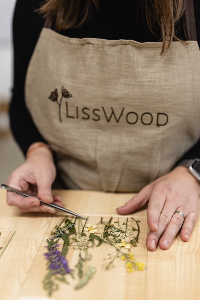 Ruce v zástěře LissWood skládají pinzetou lisované květiny